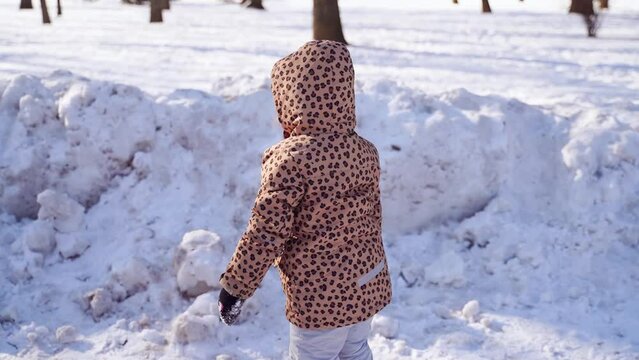 Caucasian happy preschool girl plays with snow on a sunny winter day in a park