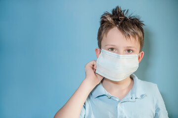 Fototapeta na wymiar boy puts on a medical protective mask on blue background. child with flu, influenza or cold protected from viruses, pollution in bad epidemic situation, among patients with coronavirus