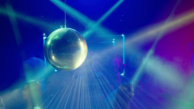 People dancing at disco, big silver disco ball above dancing floor. Nightlife, modern music and entertainment concept.