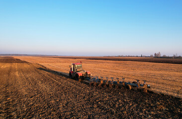 Fototapeta premium Tractor Plowing field on sunset. Red Tractor with Plough on Plowed. Ploughing and Soil Tillage. Agricultural Tractor on Cultivation Field for Sowing Seeds. Big Tractor During Field Cultivating. .