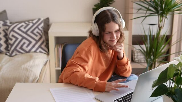 Teenage girl wears wireless headset greets teacher study online by skype, happy young woman learn language listen to lecture watch webinar on laptop, distance learning