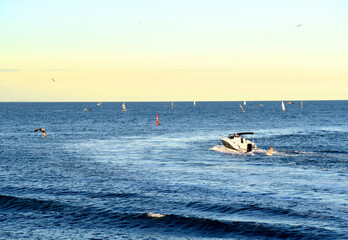 Obraz premium Motor boat in the sea at sunset. Yacht and motorboat on waves in Mediterranean Sea. Skiff and Sailboat in ocean. Yachting and sailing sport. Speedboat or powerboat on the waves near the Spanish coast.