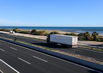 Semi-trailer truck driving along highway. Traffic on motorway and road near sea. Logistics of transportation and delivery of goods. Services and Transport logistics in a pandemic in Europe..