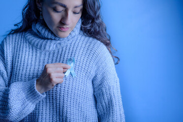 A woman's hands holding a Blue Ribbon in support of people with cancer.