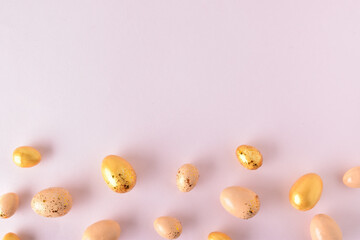 Various Easter eggs of yellow shades lie on a pink background. Easter background with painted eggs and sequins. Copy space. Flat lay, top view.