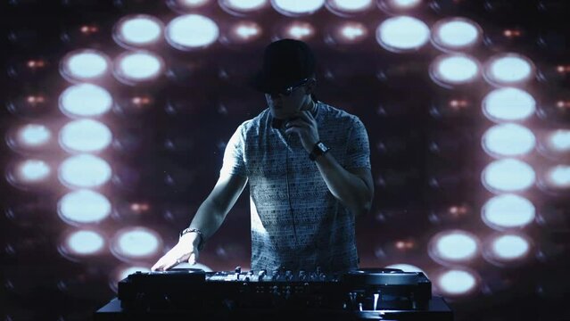 Male DJ with cap playing music, standing at mixing console and swaying to the rhythm. Nightlife, modern music and entertainment concept.