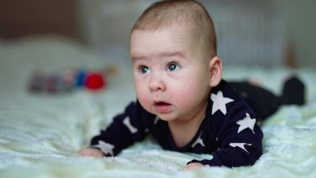 Curious and surprised little kid raised his head over the bed. Adorable baby with plump cheeks lying on belly. Close up.