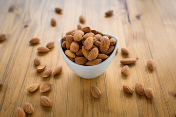 almonds in white ceramic bowl on wooden table, healthy food, plant-based food concept