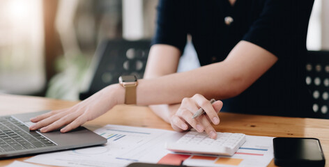 Close up Business woman using calculator and laptop for do math finance on wooden desk in office and business working background, tax, accounting, statistics and analytic research concept