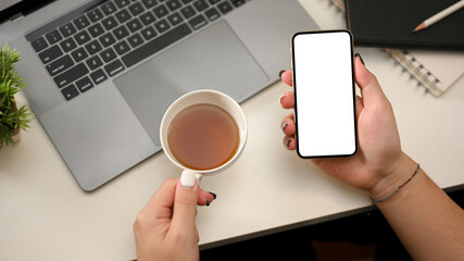 Modern office table with woman hands holding teacup and smartphone