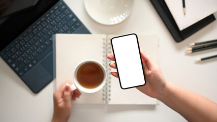 A modern minimal white workspace with a female hands holding smartphone mockup.