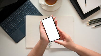 A female hands holding modern smartphone mockup over workspace.