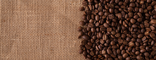 Toasted Coffee beans close up on burlap background. Panoramic image. Top view with copy space for your text.