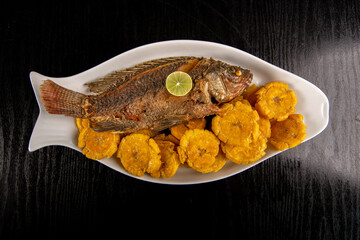Fried fish with green plantain chips (Patacones / Tostones) Photo above, black background.	