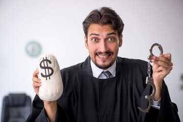 Young male judge holding moneybag in corruption concept
