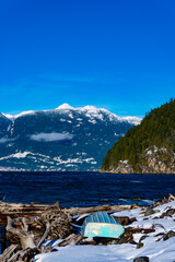 Small blue overturned boat on lakeside beach with mountains in background and blue sky