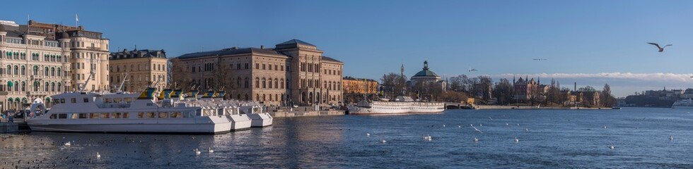 Panorama view over the bay Strömmen and the islands Blasieholmen with commuting steam boats at a pier and hotels and museums, the former military buildings and museums a sunny winter day in Stockholm