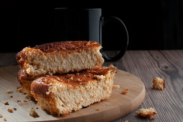Home made pieces of corn cake on a round wooden cutting board with a black background, with a black cup of coffee at the bottom, horizontal.