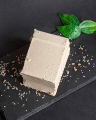 A large piece of sesame halva lies on a black serving board, a piece is cut off from the whole. National sweets, organic desserts concept, top view