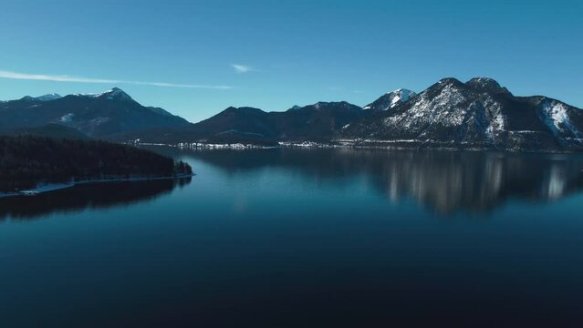 Bavarian lake Walchensee in south Germany in the idyllic alps mountains close to Austria. Blue clear drinking water waves at the white shore and idyllic blue sky in winter. 4K UHD drone aerial.