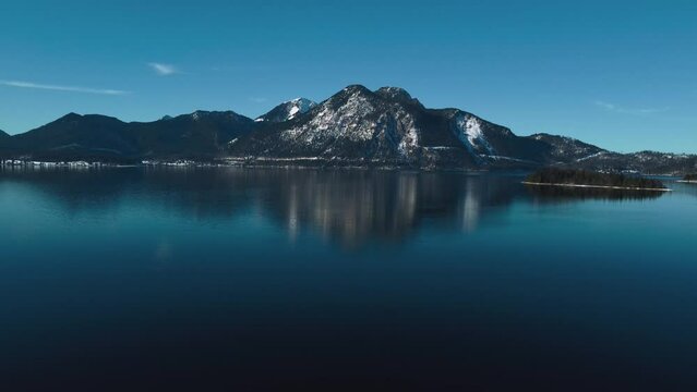 Bavarian lake Walchensee in south Germany in the scenic alps mountains close to Austria. Blue clear drinking water waves at the white shore and blue sky in winter. 4K UHD drone aerial.