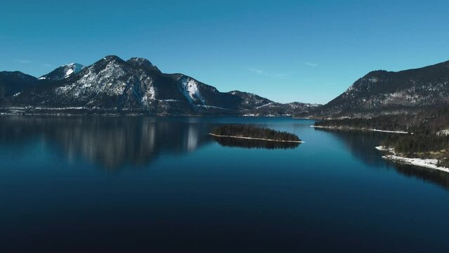 Bavarian lake Walchensee in south Germany in the scenic alps mountains close to Austria. Blue clear drinking water waves at the white shore and idyllic blue sky in winter. 4K UHD drone aerial.
