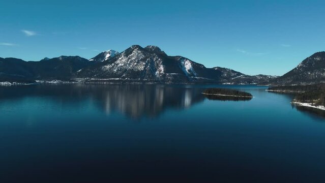 Bavarian lake Walchensee in south Germany in the alps mountains close to Austria. Blue clear drinking water waves at the white shore and idyllic blue sky in winter. 4K UHD drone aerial.