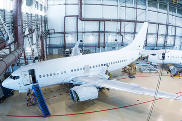 White passenger jet planes in the hangar. Airliners under maintenance. Checking mechanical systems for flight operations
