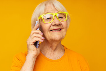 Portrait of an old friendly woman fun talking on the phone yellow background