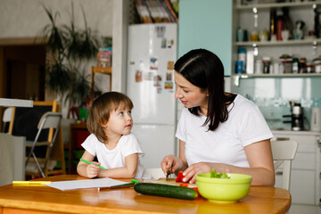 Mother and little daughter sitting in the kitchen, making salad, drawing. Happy family concept. Daily home life