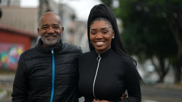 A black father and a teen daughter walking together outside during drizzle rain