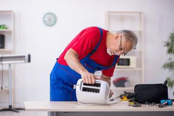 Old repairman repairing toaster at workshop