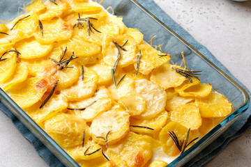 Step-by-step recipe of potato gratin with rosemary in glass baking dish on blue napkin. Potato casserole