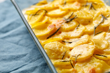 Potato gratin with rosemary and cheese in glass baking dish on blue napkin. Step-by-step recipe. Potato casserole