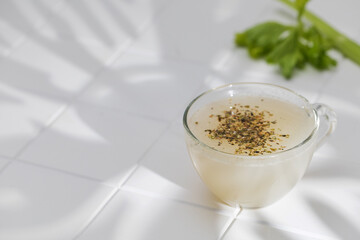 Healthy bone broth with spices in a mug on a white tile with a shadow pattern. 