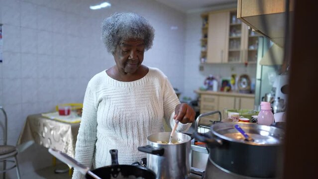 A black older woman cooking at kitchen stirring por