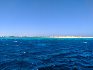 Beautiful view of the bright red sea and hotel buildings on the horizon against the blue sky. Copy space. Hurghada, Egypt.