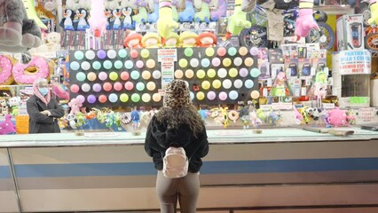 GIrl shooting with darts on multicoloured balloons in Valencia funfair - back view