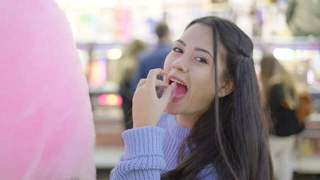 Brunette teenage girl eating pink colour cotton candy in an amusement park - close-up slow-motion