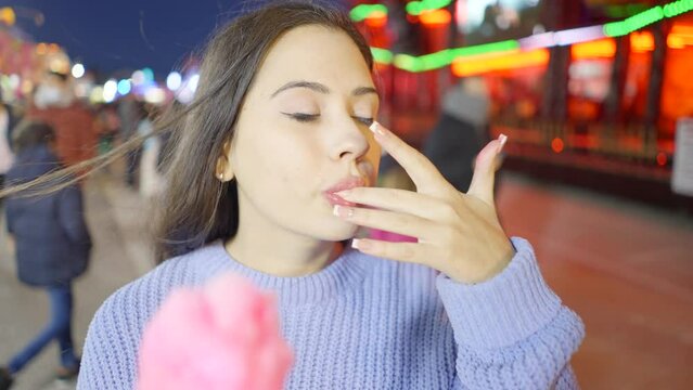 Face close-up of a girl licking and sucking sticky sugary fingers after eating candy floss in a country fair at night