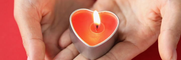 In female hands burning candle in form of heart