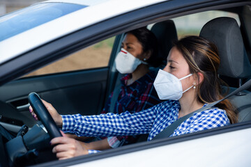 Two women in protective medical masks in a car interior