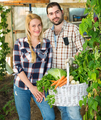 Fototapeta premium Cheerful couple of farmers holding baskets of harvest at garden