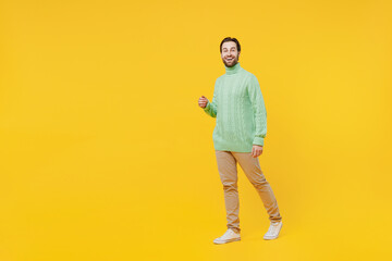 Full body smiling happy young caucasian man 20s wearing mint knitted sweater walking going strolling look camera isolated on plain yellow background studio portrait. People lifestyle fashion concept.