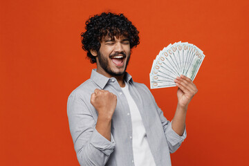 Young bearded Indian man 20s years old wear blue shirt holding fan of cash money in dollar...