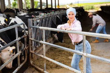 Confident woman farmer standing near cow and man working on background at farm