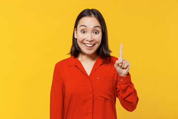Insighted smart proactive beautiful fun young woman of Asian ethnicity 20s years old wears orange shirt holding index finger up with great new idea isolated on plain yellow background studio portrait.