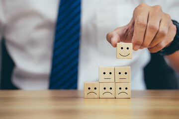 Closeup hands holding smiley face icon on wooden cube, service rating, leadership and corporate...