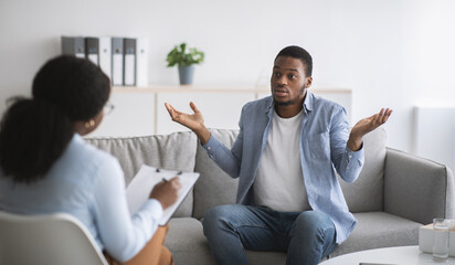 Puzzled young black guy having session with psychologist at mental health office
