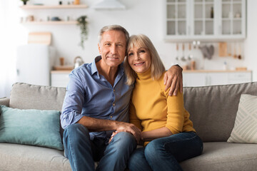 Loving Senior Couple Hugging Sitting On Sofa Posing At Home